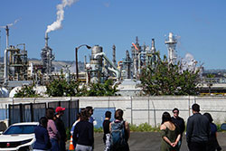 people outside fenced factory with smoke plumes