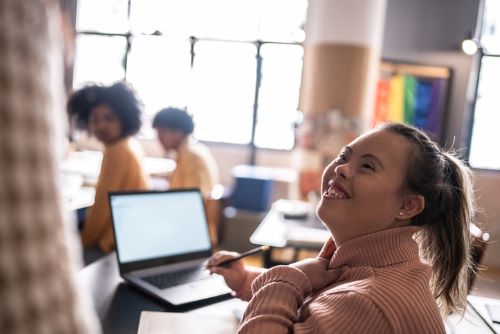 Woman with intellectual and developmental disabilities with a laptop in a classroom, smiling and talking