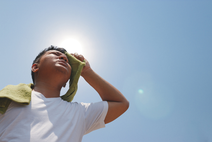 man outside in sunlight experiencing heat stroke, wiping face with towel